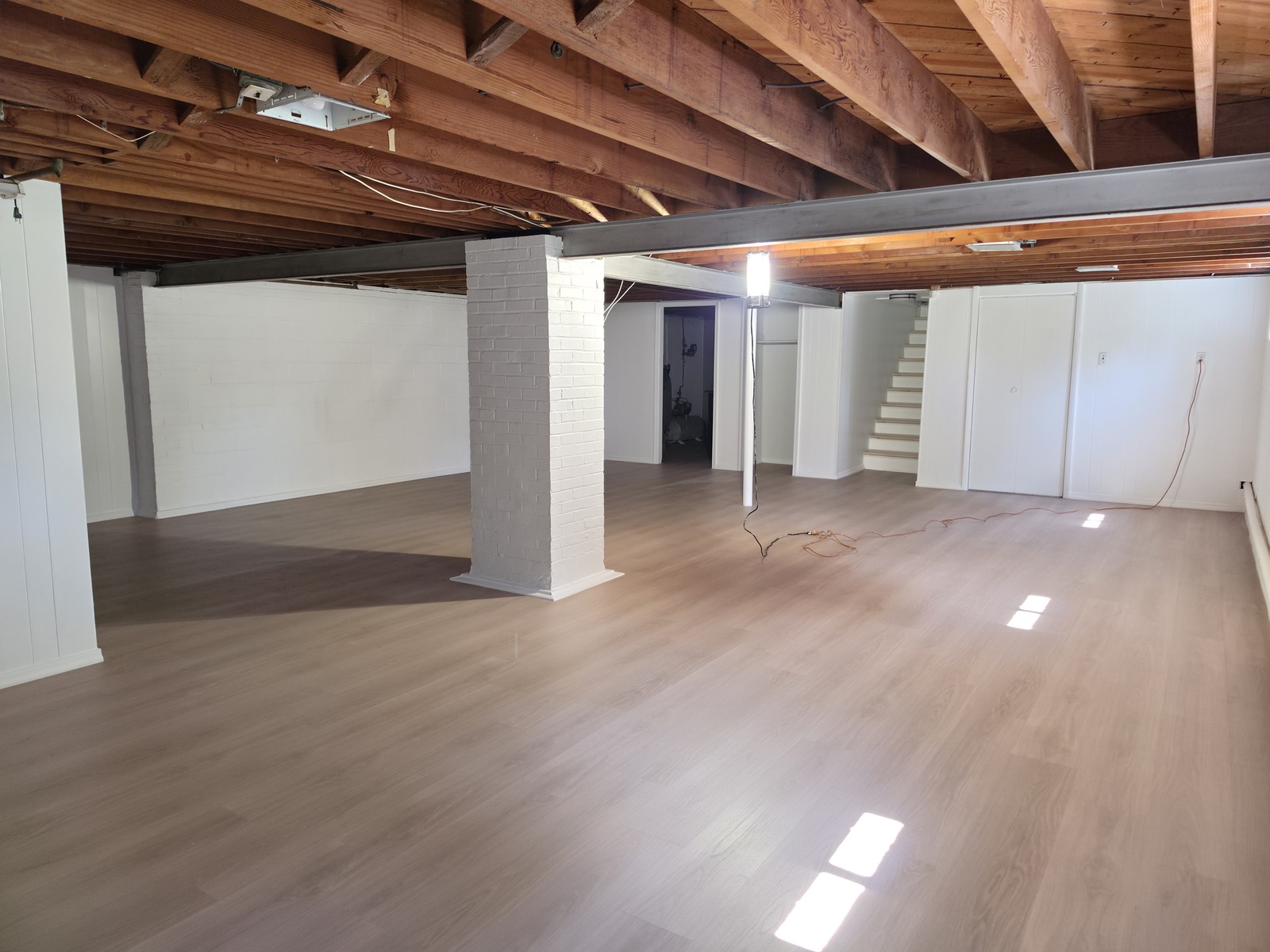 New LVP flooring in the featured home's basement, with white masonry walls, columns and exposed ceiling joists