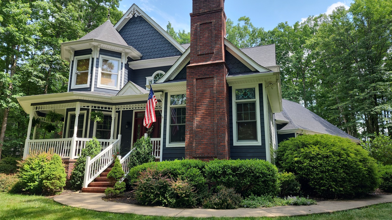 Blue house exterior with white architectural trim, a front porch and brick chimney