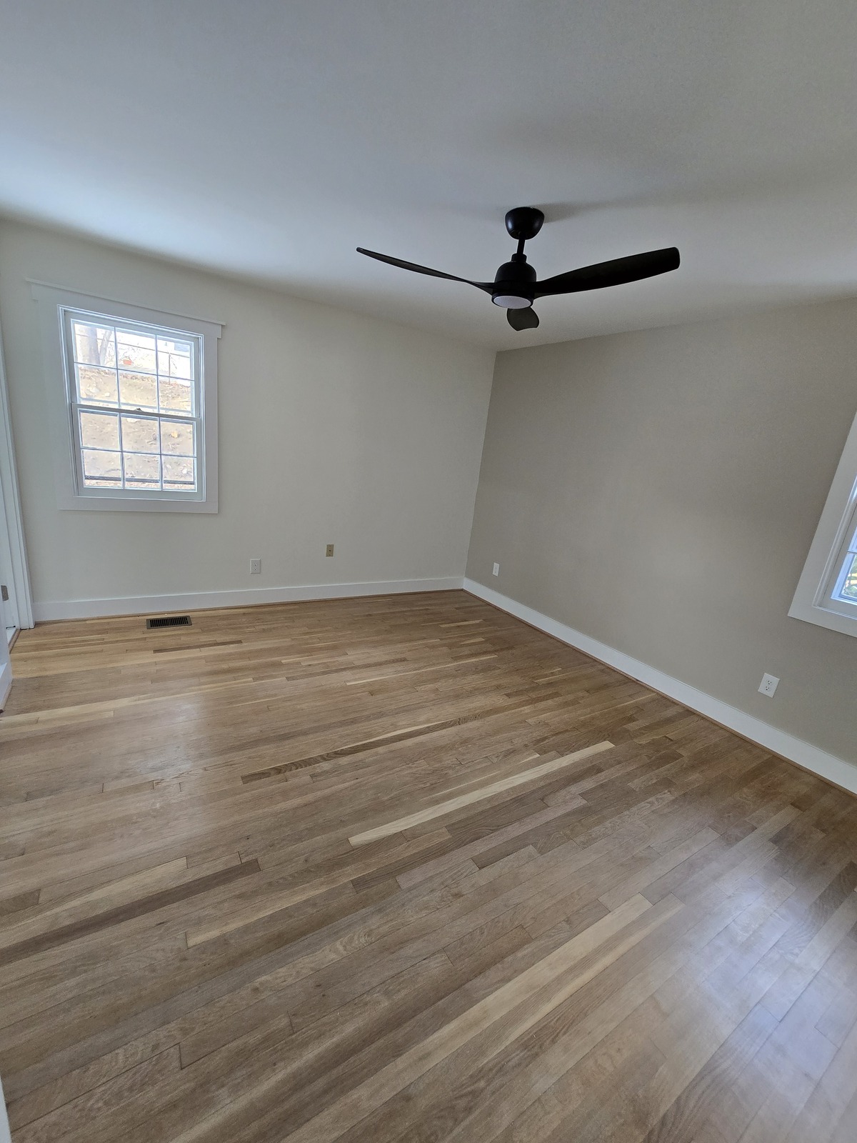 Neutral painted bedroom with a natural wood floor and white baseboards
