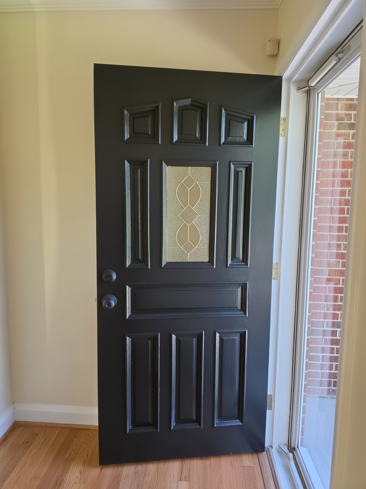 Black paneled entry door with decorative glass, white trim and cream-painted surrounding walls