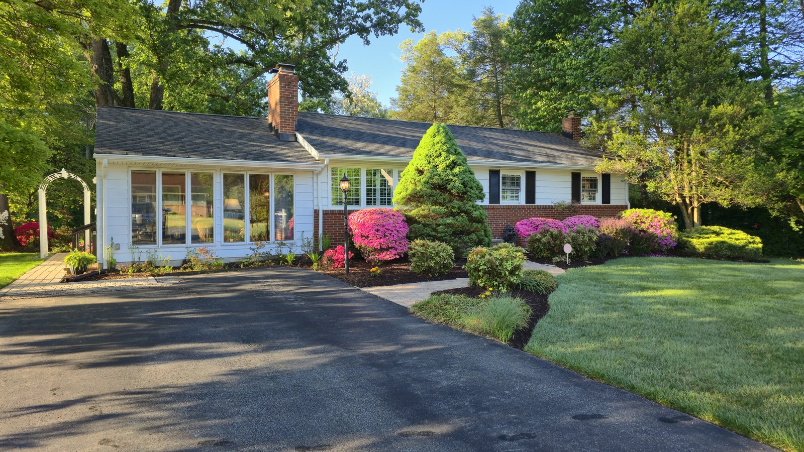 House with white siding, brick, black shutters and landscaping